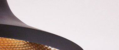 Photographie présentant un détail d'une lampe en suspension. Lampe Beat Light Wide, de Tom Dixon, en laiton noir mat et doré.