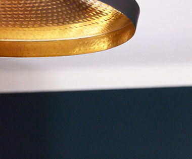 Photographie présentant un détail d'une lampe en suspension. Lampe Beat Light Wide, de Tom Dixon, en laiton noir mat et doré.