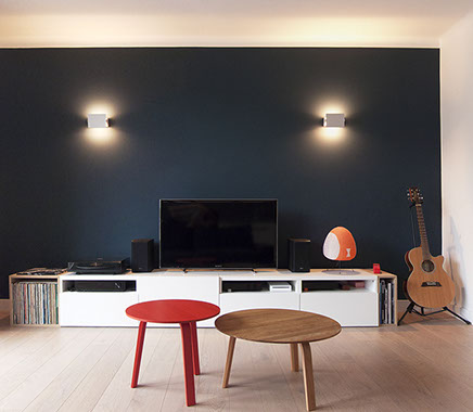 Salon avec un mur bleu sombre Farrow and Ball et 2 appliques 1962 de Charlotte Perriand. Parquet en chêne massif. 2 tables basse Bella de Hay. 