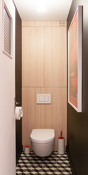 WC suspendue avec chasse d'eau et placar dissimulés derrière un habillage en hêtre. Sol en carreaux de ciment, effet géométrique noir et blanc.