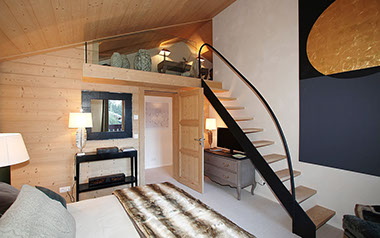 Chambre principale du chalet avec mezzanine et escalier leger en bois et métal.