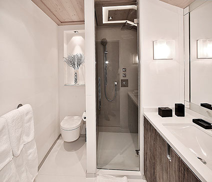 Salle de bains d'une chambre du chalet. Sol en pierre, grand miroir au dessus du meuble lavabo avec plan de travail en pierre et porte en chêne.