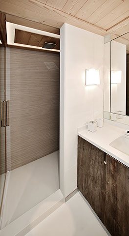 Salle de bains d'une chambre du chalet. Sol en pierre, grand miroir au dessus du meuble lavabo avec plan de travail en pierre et porte en chêne.